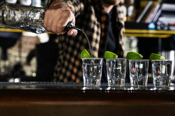 Bartender pouring Mexican Tequila into shot glasses at bar counter, closeup