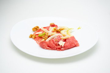 albese meat with savoy cabbage, walnuts, celery and parmesan cheese in the foreground on plate and white background