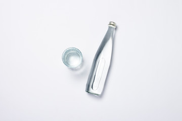 Bottle of pure crystal water and glass on a white background under sunlight. Banner. Concept of thirst, heat, summer, tropic. Flat lay, top view