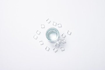 Glass of pure crystal water and ice cubes on a white background under sunlight. Banner. Concept of thirst, heat, summer, tropic. Flat lay, top view