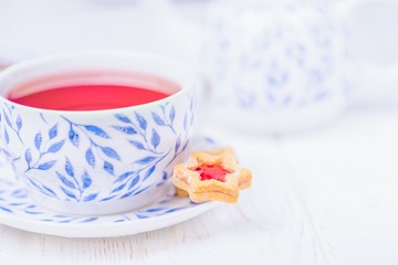 Pink fruit tea and homemade cookie star with jam on a white wooden background