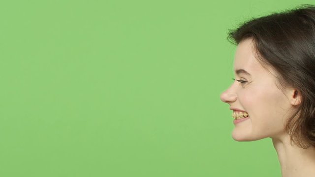 Slow-motion profile portrait of happy, sincere and enthusiastic lovely young short-haired woman, wear braces, smiling and looking left blank green background, chuckle joyfully, grinning beaming face
