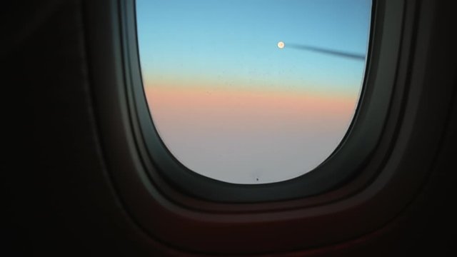 Focus on a porthole glass with ice crystals and hot gases from the engine. Wing of passenger airplane passenger pov through plane window during flight. Aircraft above clouds. Air travel concept.