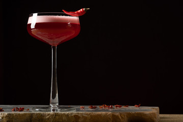 Red cocktail with foam, black background.