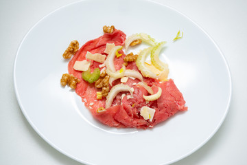 albese meat with savoy cabbage, walnuts, celery and parmesan cheese in the foreground on plate and white background