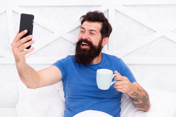 Blogging from bed. Happy blogger drink coffee in morning. Bearded man keep real time live blog....