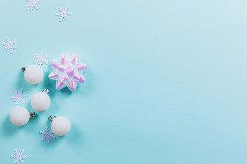 Blue background with white Christmas decorations and holographic bow. Holiday concept. Flat lay, copy space