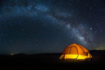 Lit tent on the playa under a bright Milky Way arch of stars