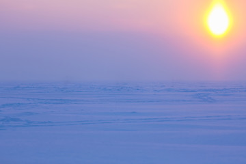 Winter evening landscape with a sun disk in the sky. Natural winter background. Beautiful winter sunset at ice desert