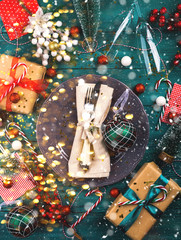 Christmas dark green still life background with festive tableware and celebration ornament around, gift boxes. Holiday new year dinner lunch flat lay concept. Falling snow, magic lights effect