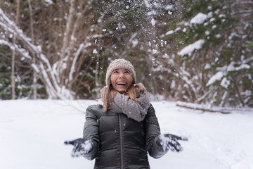 Happy woman catching snowflakes on the walk in snowy winter forest. Spending vacations outdoor,...