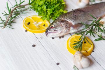 Fresh trout on white table with parsley , garlic and rosemary. Tasty fish prepare for eating.