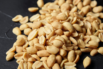 Roasted peeled peanuts closeup, salty beer snack scattered on black stone background
