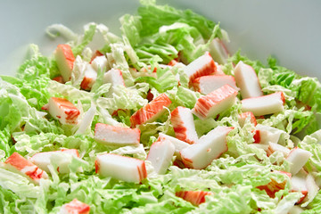 Pieces of crab sticks and fresh chinese cabbage leaves chopped in white ceramic bowl on black stone background. Green vegetable and imitation crab meat, sea food.  Cooking salad