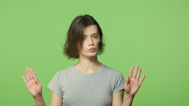 Slow-motion, denial and rejection concept. Young strict, determined short-haired woman shake head in refusal, no gesture, raise hands stop, hold and prohibit action, make cross sign, green background