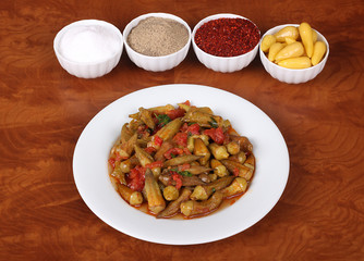 the one  Okra with red pepper and turkey spices on white plate on wooden bamya table for Hotel & Restaurant Orders and Menu and Internet and TV