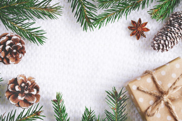 Obraz na płótnie Canvas Christmas composition of pine tree branches, pinecones, presents in craft paper and anise stars on white knitted fabric as a background with copy space. Flat lay style.
