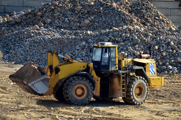 Obraz na płótnie Canvas Large heavy front-end loader or all-wheel bulldozer for mechanization of loading, digging and excavation operations in open quarry. Crusher plant with belt conveyor, crushing process, grinding stone