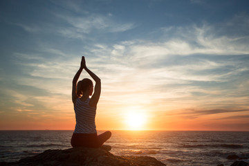 Yoga silhouette woman in meditation on the ocean beach during amazing sunset.
