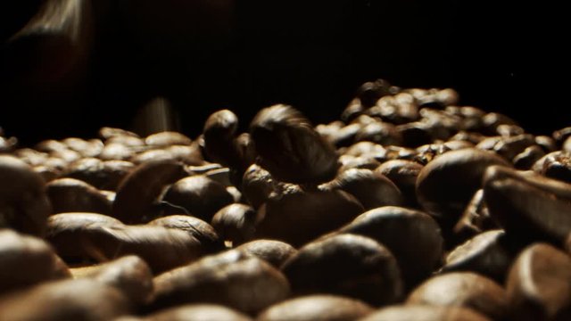 Close Camera movement through falling fresh coffee beans into a pile of beans laying on a wooden surface
