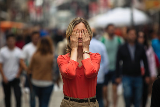 Woman covers his eyes during panic attack in public place.