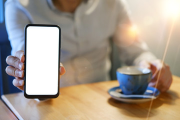 close-up of man hands showing smartphone's blank screen and holding coffee mug over the table