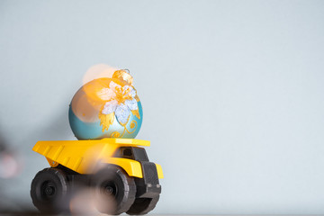 Yellow dump truck model with Christmas tree toy. Garland lights in defocus.