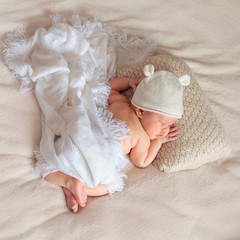 Portrait of cute sleeping newborn baby in white knitted hat in light bedroom. Family, motherhood, love, health, innocence and care