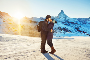 Happy travelers couple man and woman trekking in Swiss Alps, enjoy beautiful sunset view of Matterhorn mountain, kiss. Explorers hiking, travel in Switzerland. Romantic holidays outdoors on nature.