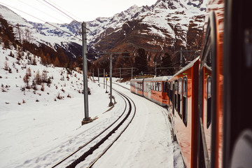 Alpine Swiss train going to the snowy Matterhorn mountain in winter. Tourists travel to mountain ski resort on railway transport from Zermatt village, Switzerland, Alps. Glacier express on the way.