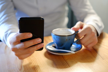 close-up of man hands using smartphone and holding coffee mug and planning book over the table