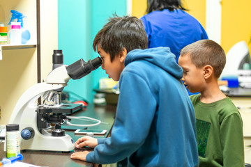 The boy looks through a microscope in a laboratory with curiosity.  Children came on an excursion to the clinic.