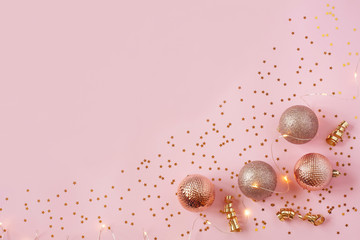 Christmas pink bauble, lights, gold serpentine and confetti on pastel pink background. Christmas, New Year, winter holiday concept. Flat lay, top view, copy space.