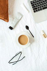 Fototapeta na wymiar Morning breakfast with coffee in bed with white linen. Flat lay fashion, beauty background with laptop, cosmetics. Top view freelancer concept for blog, magazine, social media. Concealer, lipstick.
