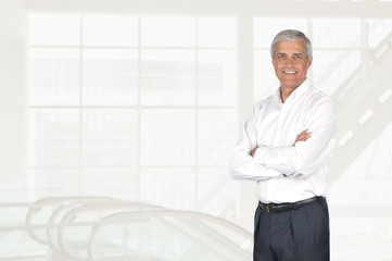 Mature businessman portrait with his arms folded, in high key modern office setting.