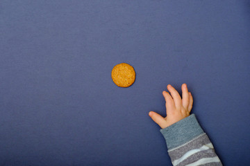Child hand reaching for cookie on the table. Baby taking a food, tasty sweets for kids.