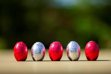 A portrait of five colorful and shiny easter eggs in their wrapping standing up on a table for children to find.