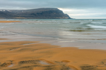 Fototapeta na wymiar Raudasandur or red sandy beach in the westfjords of Iceland during blue hour. Waves crash into the red sandy dunes at low tide. Texture in the foreground and mountains in the background. 