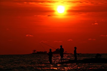 Silhouette of fishermans on the beach at sunset