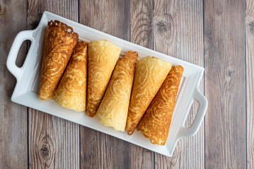 Norwegian Krumkake cookies on a white ceramic plater, rustic wood background