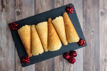 Norwegian Krumkake cookies on a slate plater, rustic wood background, red bows and bells