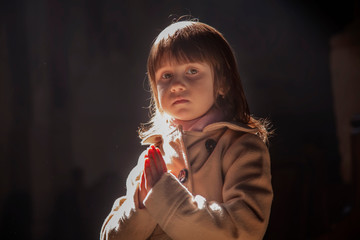 Little child girl praying in the church in in the rays of the sun.