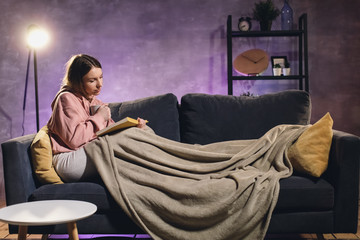Young girl reading a book. The girl is lying on the couch. Cozy room. Girl dreams