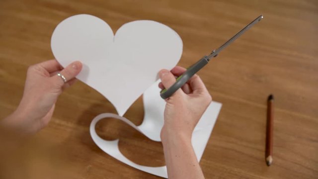 a young woman draws a heart on a white paper and then cuts it with scissors. Production of gifts out of love