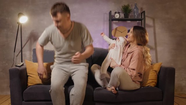 Young family sitting on the couch in a cozy room. Mom, dad and baby play together. Family happy