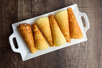 Norwegian Krumkake cookies on a white ceramic plater, rustic dark wood background