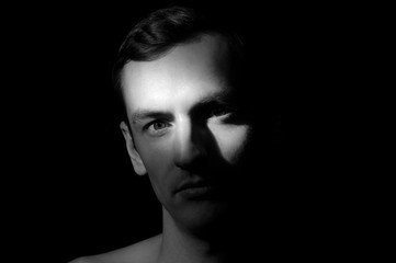 black and white dramatic portrait of a guy close-up on a black background with one light source