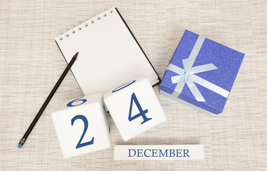 Cube calendar for December 24 and gift box, near a notebook with a pencil