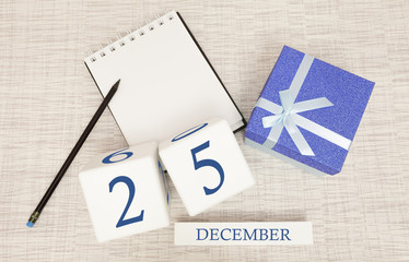 Cube calendar for December 25 and gift box, near a notebook with a pencil