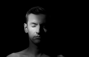 black and white dramatic portrait of a guy close-up on a black background with one light source